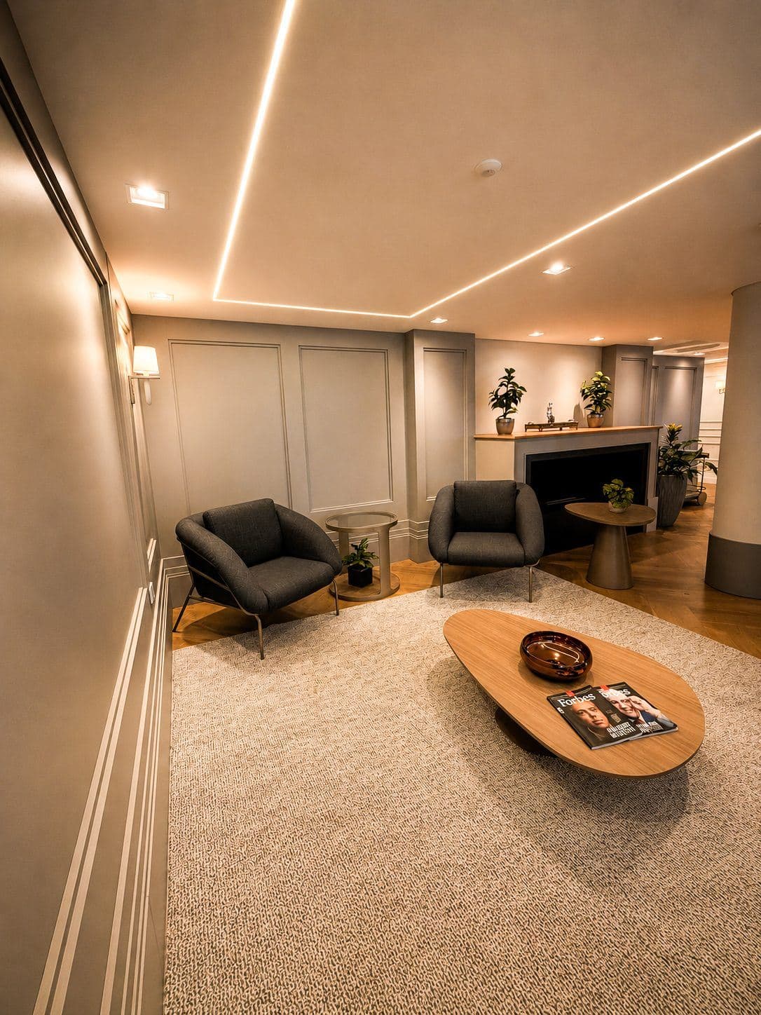 MYJOB Afonso Pena: estar com duas poltronas cinza, mesa de centro oval de madeira com revistas, lareira decorativa com plantas, paredes em boiserie e frisos de luz no teto