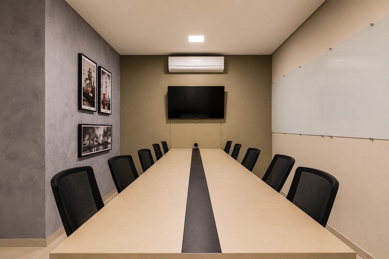 MYJOB Dourados: sala de reunião com mesa longa clara, cadeiras pretas, TV na parede do fundo, quadro de vidro e quadros de Londres